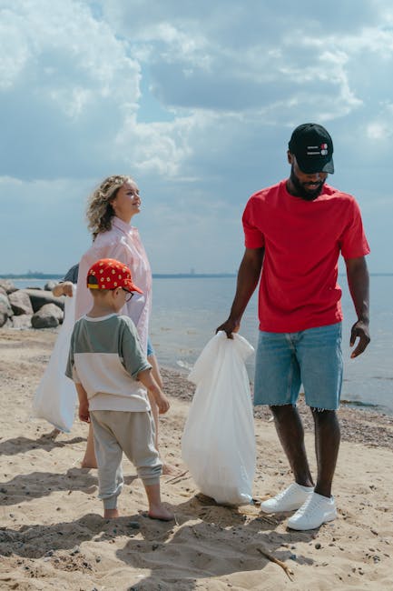A man wearing a beige cap, glasses, and a light-colored long-sleeve shirt is walking outdoors during the daytime, carrying a green plastic bag filled with waste in his left hand and holding an orange 